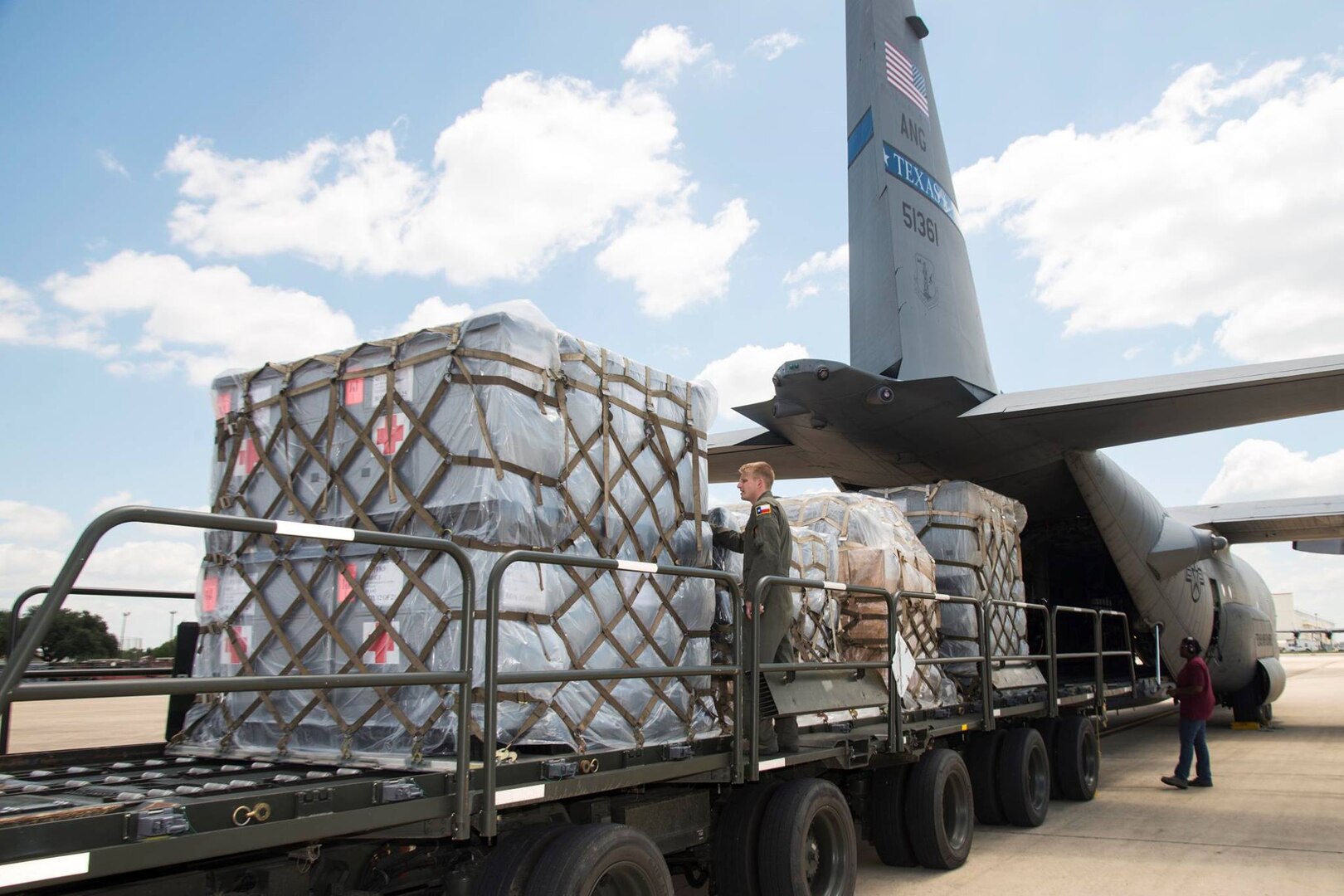 Pallets of supplies on flatbed trailer being loaded onto C-130 cargo plane