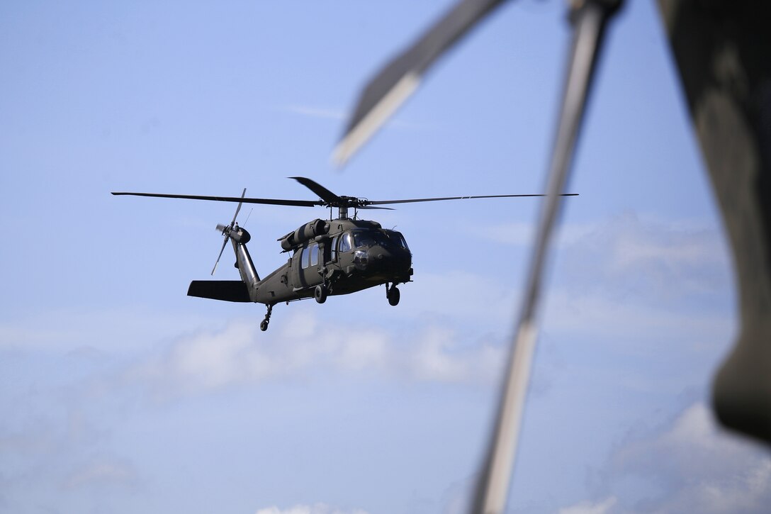 An Army UH-60 Black Hawk helicopter flies by as soldiers prepare another helicopter to depart Joint Base McGuire-Dix-Lakehurst