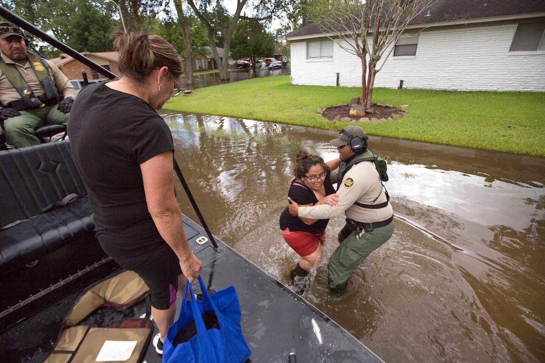 A Border Patrol riverine agent standing in calf-deep flood waters helps a woman to board an air boat during search and rescue operations