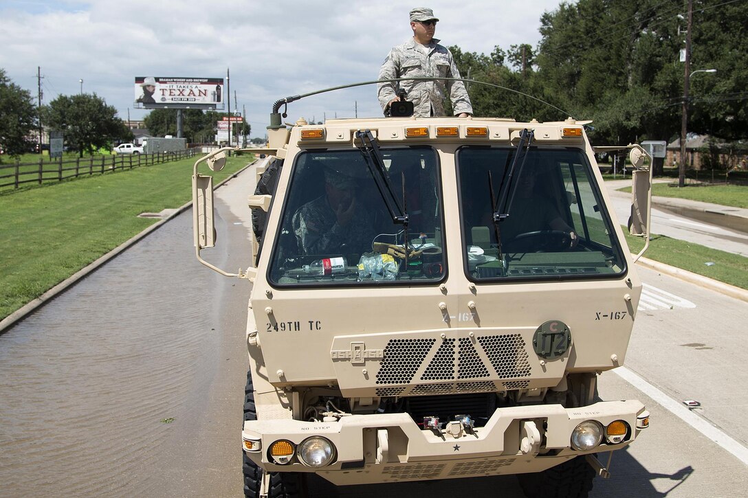 An airman stands atop a light medium tactical vehicle in a roadway.