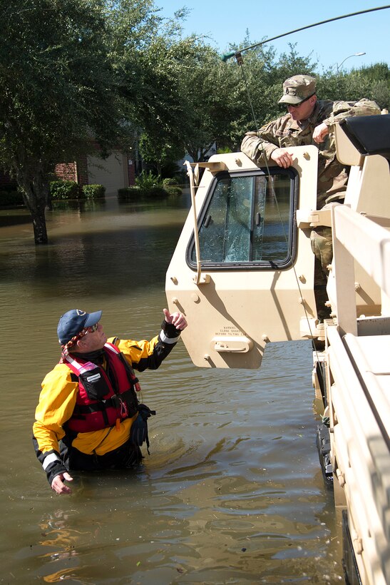 A soldier in a military vehicle talks to a rescuer standing by the vehicle in waist-deep waters.