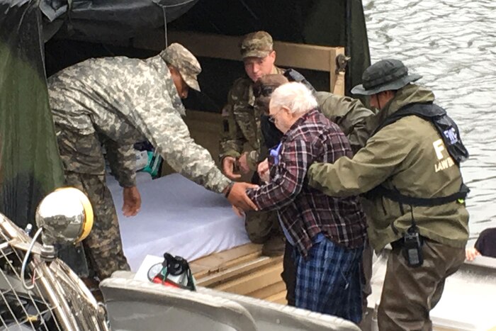 A group of people help a man into the back of a military vehicle.