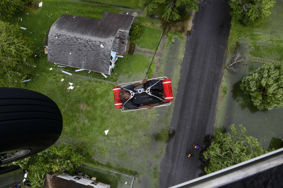 A helicopter hoists a resident lying in a basket up to a helicopter during a rescue.