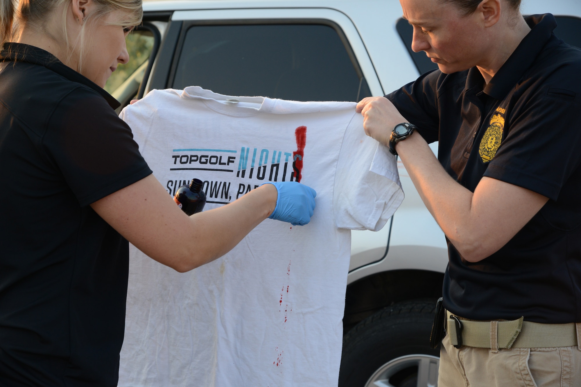 A special agent from Malmstrom’s Office of Special Investigations holds a t-shirt while a forensic science agent from Buckley Air Force Base, Colo., spreads fake blood to simulate evidence for a training exercise Aug. 29, 2017, at Malmstrom Air Force Base, Mont. The forensic science agent trained OSI and public affairs teams from Malmstrom on processing a crime scene. (U.S. Air Force photo/Staff Sgt. Delia Martinez)