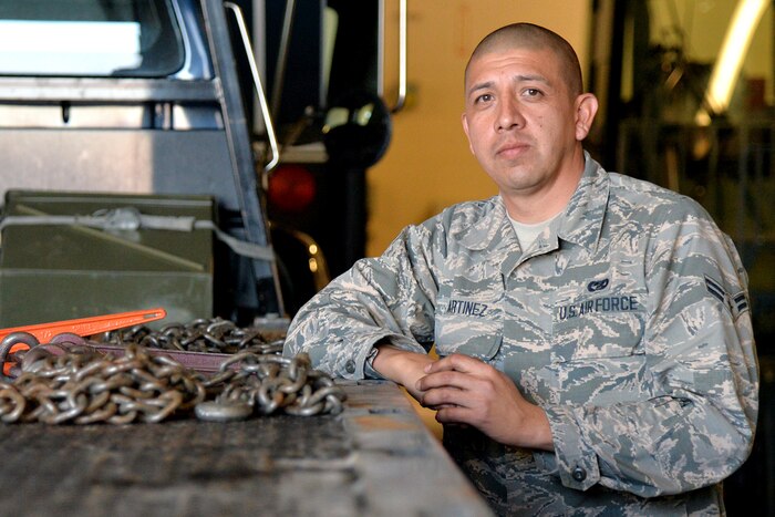 An airman poses for a photograph next to a truck.