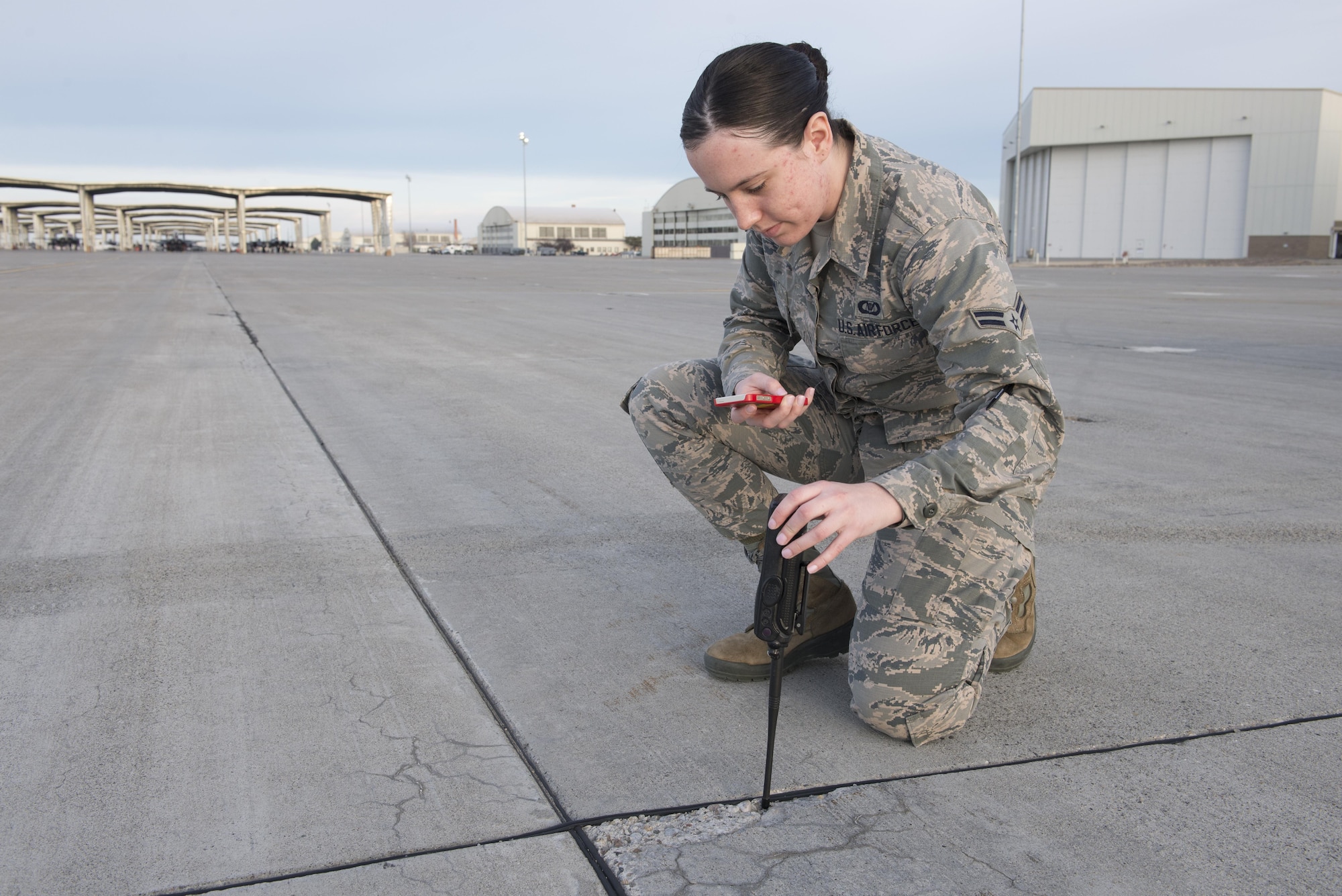 Airman 1st Class Sabrina Watson, 366th Operations Support Squadron airfield management coordinator takes a photograph of a crack in the runway Nov. 30, 2017, at Mountain Home Air Force Base, Idaho. Once completing checks for cracks or debris on the runway the information is tracked in a log and submitted to the 366th Civil Engineer Squadron to be fixed. (U.S. Air Force photo by Senior Airman Lauren-Taylor Levin)