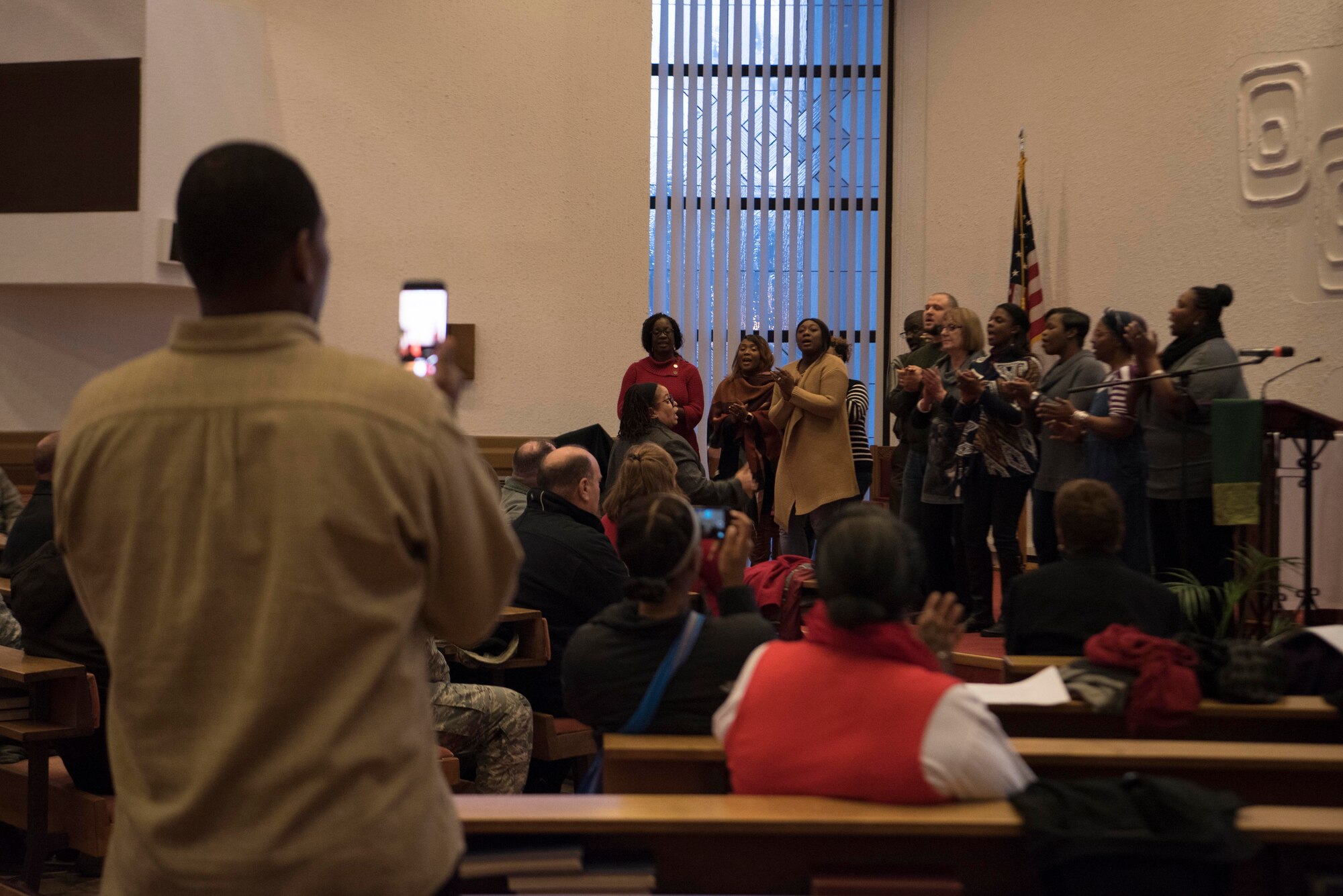 Members of the Ramstein combined choir sing Christmas carols as a member records video during the base Christmas tree lighting ceremony at Ramstein Air Base, Germany, Nov. 29, 2017. Members gathered at the Northside Chapel before going outside to watch the tree light up. (U.S. Air Force photo by Airman 1st Class Devin M. Rumbaugh)