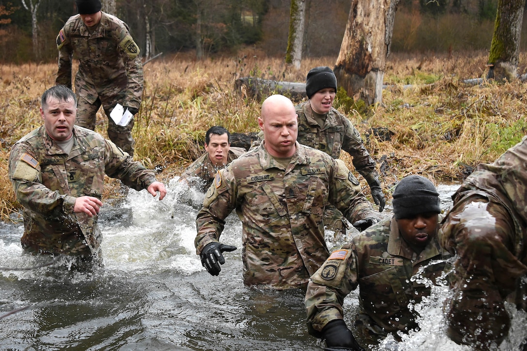 Soldiers wade across waist-high waters in a creek.