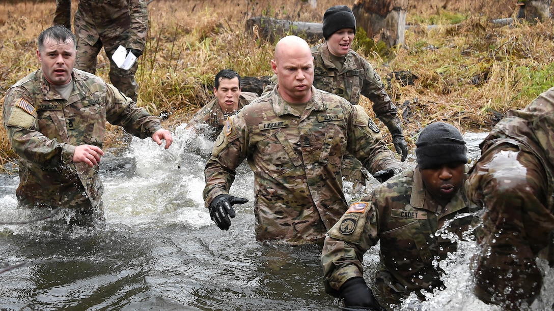 Soldiers wade across waist-high waters in a creek.