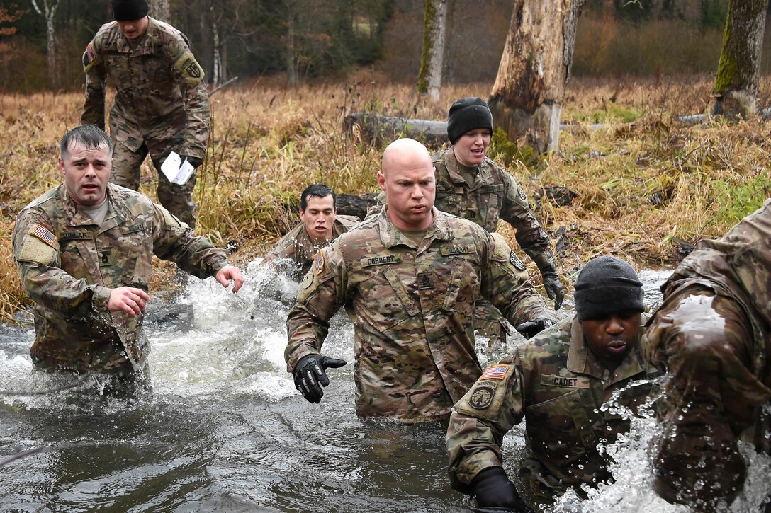 Soldiers wade across waist-high waters in a creek.