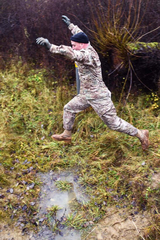Army Maj. Corey Warren jumps over a water-ditch obstacle.