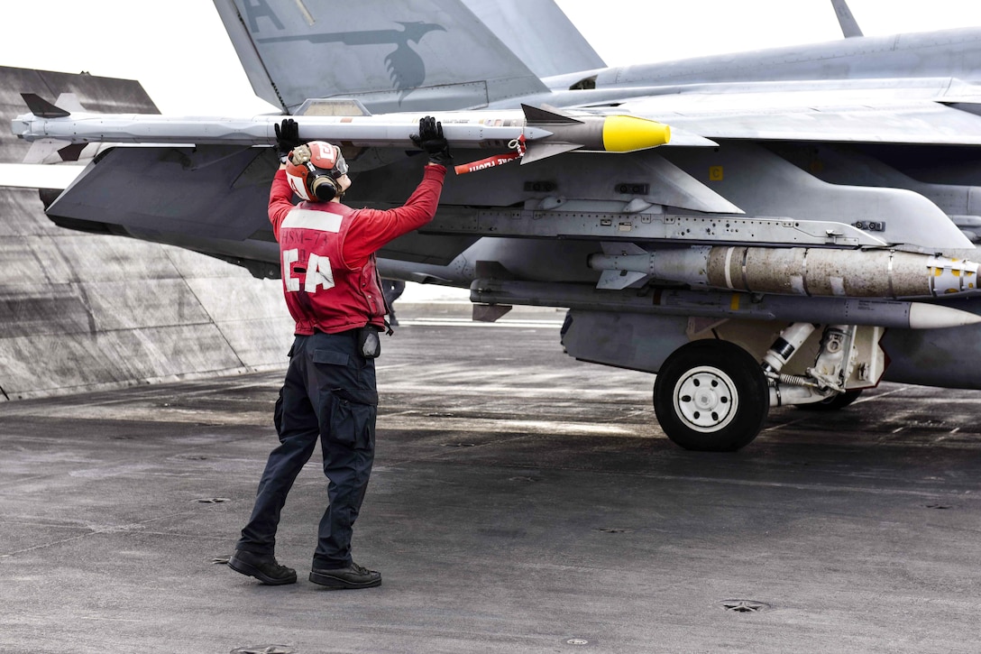 Navy Petty Officer 3rd Class Austin Renkiewicz ensures ordnance is properly secured to an F/A-18F Super Hornet aircraft.