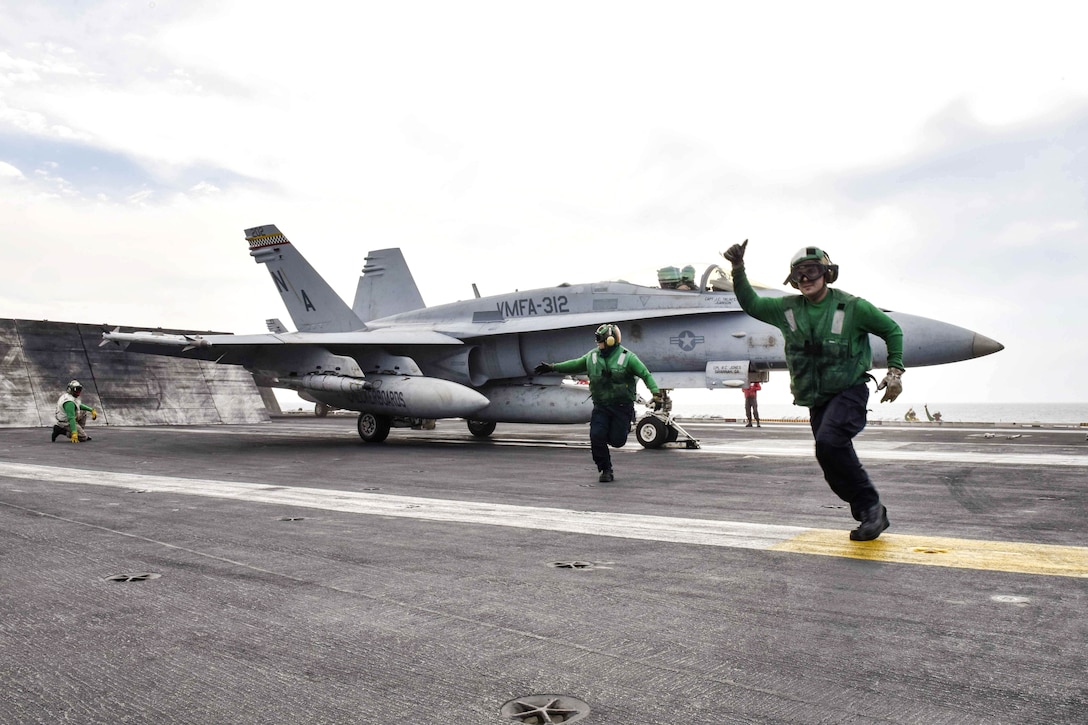 Sailors run as they signal an F/A-18C Hornet aircraft is ready to launch.