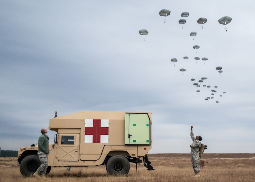 An Army ambulance in the foreground, airborne soldiers descend