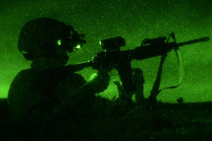 A service member wearing night vision goggles reloads an M4 carbine rifle during night-fire training at Joint Base San Antonio-Camp Bullis.