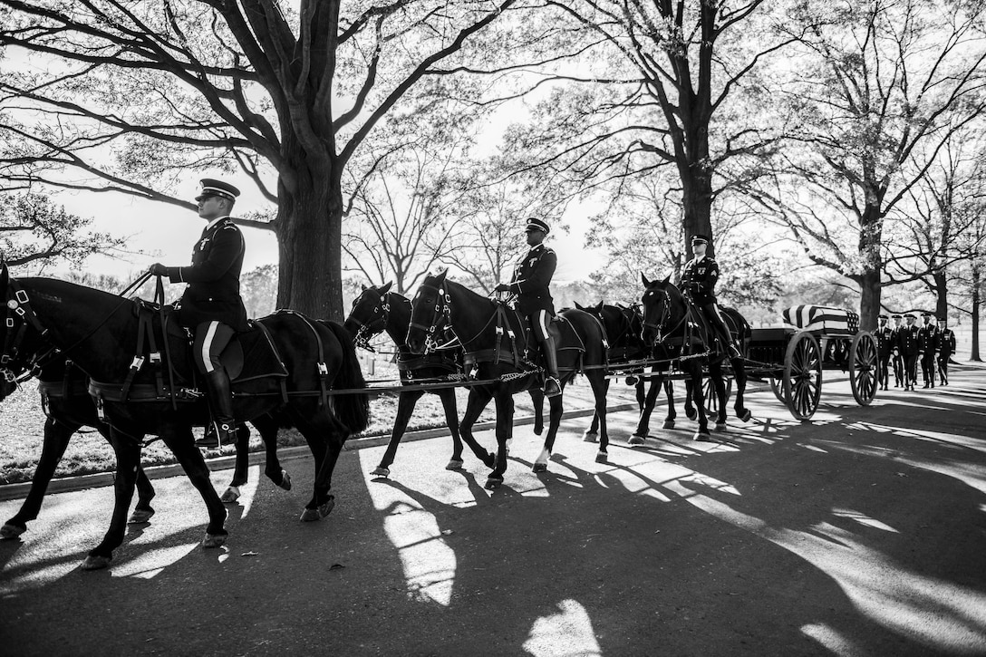 Soldiers on horseback lead a funeral procession.