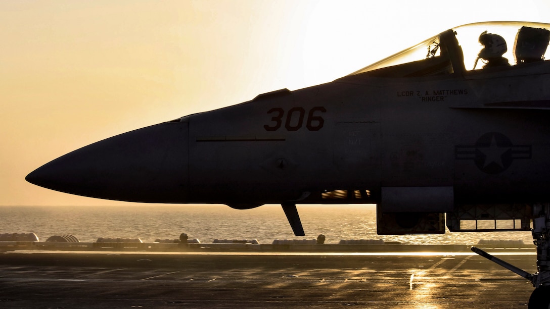An aircraft, shown in silhouette, taxis on a ship's flight deck.
