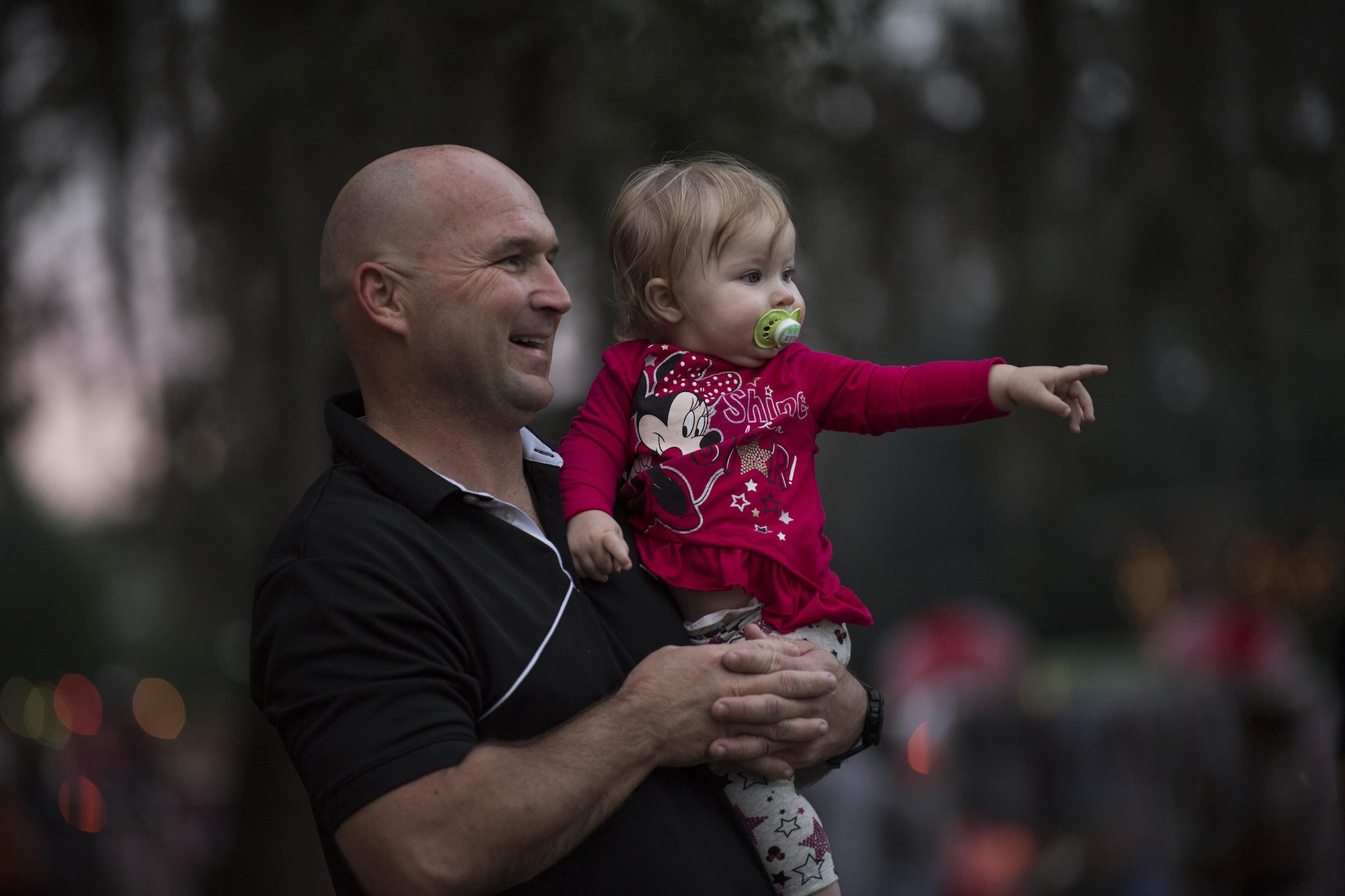 Senior Master Sgt. Matt Jenkins, 23d Maintenance Group weapons standardization section superintendent, watches the parade with daughter Etta, Dec. 1, 2017, at Moody Air Force Base, Ga. The annual event brings the base community together as a way to show thanks for their continuous sacrifice and celebrate the holiday season. The celebration included a parade, raffle give-a-ways, children’s activities and traditional lighting of the base Christmas tree by families of deployed Airmen. (U.S. Air Force photo by Andrea Jenkins)