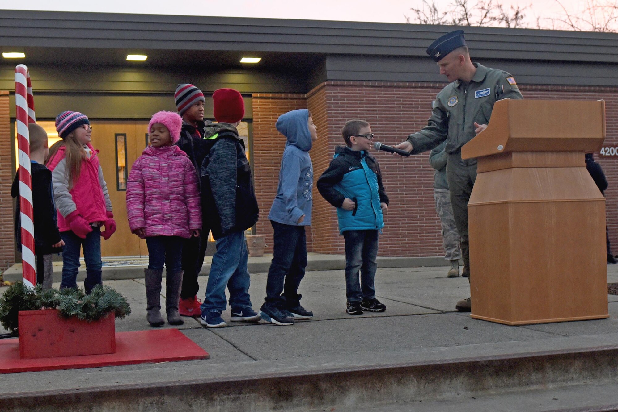 Col. Ryan Samuelson, 92nd Air Refueling Wing commander, welcomes Michael Anderson Elementary students to the stage to call for Santa Claus during the annual Holiday Tree Lighting Ceremony Dec. 1, 2017, at Fairchild Air Force Base, Washington. Children with deployed parents were asked to join Samuelson on stage to welcome Santa Claus to the base chapel to light the tree. (U.S. Air Force photo/Airman Whitney Laine)