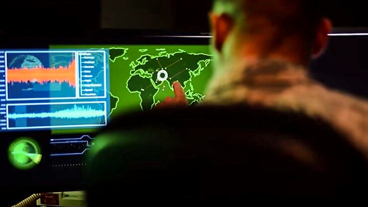 A service member, shown from behind, points to a site on a map illuminated on a monitor.