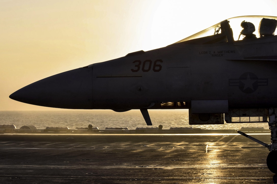 An aircraft, shown in silhouette, taxis on a ship's flight deck.