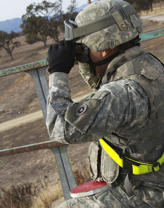 Spc. Alexis Nunez uses binoculars to observe target locations of rounds fired down range from an M240B machine gun.