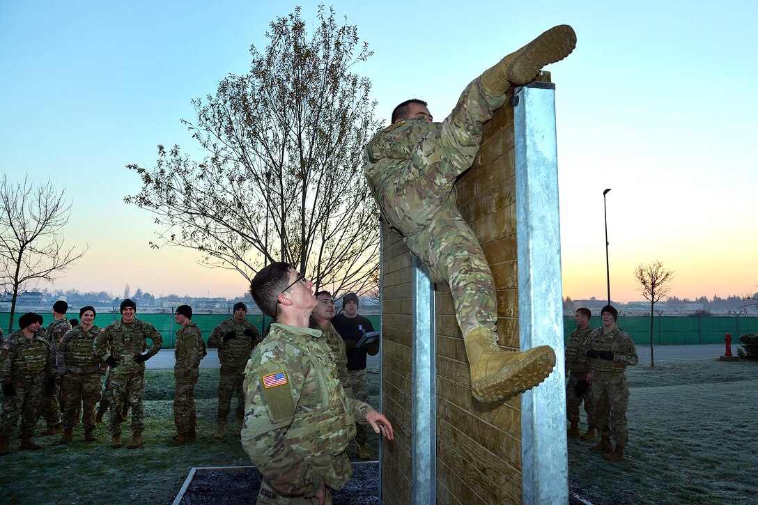 A soldier climbs over the vertical wall obstacle during physical training.