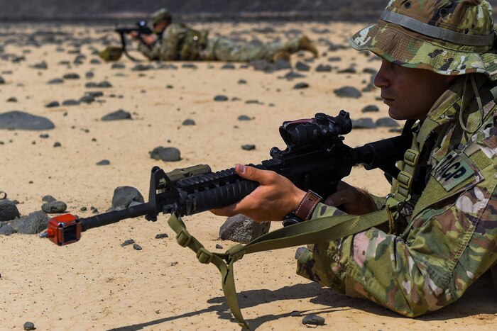 Two soldiers holding weapons take position on a beach.