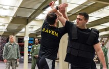 Brig. Gen. Steven Bleymaier, Director of Logistics, Engineering and Force Protection, Headquarters Air Mobility Command, Scott Air Force Base, Ill., and Master Sgt. Brian Goring, 436th Security Forces Squadron Ravens NCO in charge, watch a Ravens demonstration Nov. 30, 2017, on Dover Air Force Base, Del. Ravens Senior Airman Kirk Salvage, center, blocks a training knife attack by Senior Airman Nicholas Christopher, right, during a simulated hostile attack. (U.S. Air Force photo by Roland Balik)