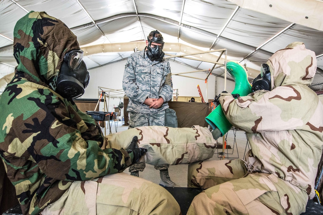 Airman Collin Barnett, center, instructs airmen how to remove contaminated gear during a joint chemical hazard training exercise.