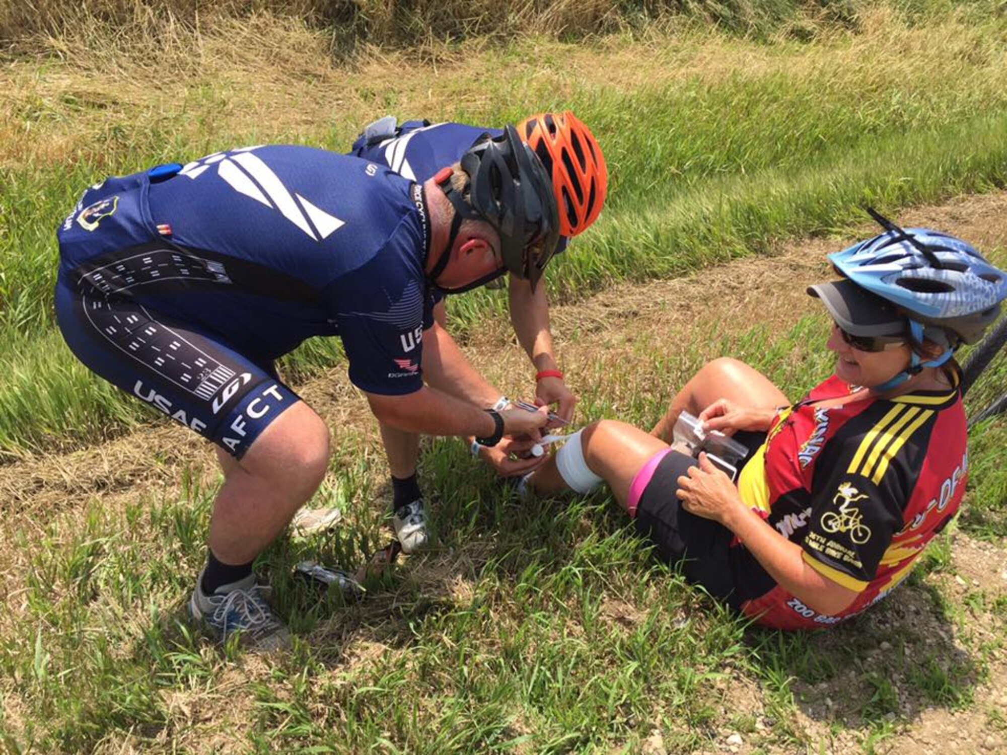 Members of the Air Force Cycling Team help an injured cyclist after she fell during the Register's Annual Great Bike Ride Across Iowa, in Charles City, Iowa, July 27, 2017. During the RAGBRAI, AFCT members provided assistance to more than 5,000 cyclists. The team works to promote the Air Force by interacting with the American public at cycling events across the United States. (Courtesy Photo)