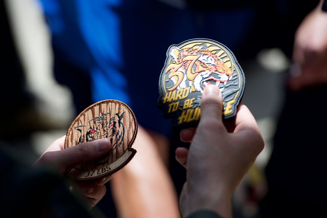 A U.S. Air Force B-1B Lancer pilot with the 37th Expeditionary Bomb Squadron, Andersen Air Force Base, Guam, holds up squadron patches featuring the squadron’s deployment mascot to an Australian visitor during an aircraft static display on Dec. 1, 2017, at Royal Australian Air Force (RAAF) Base Amberley, Australia.