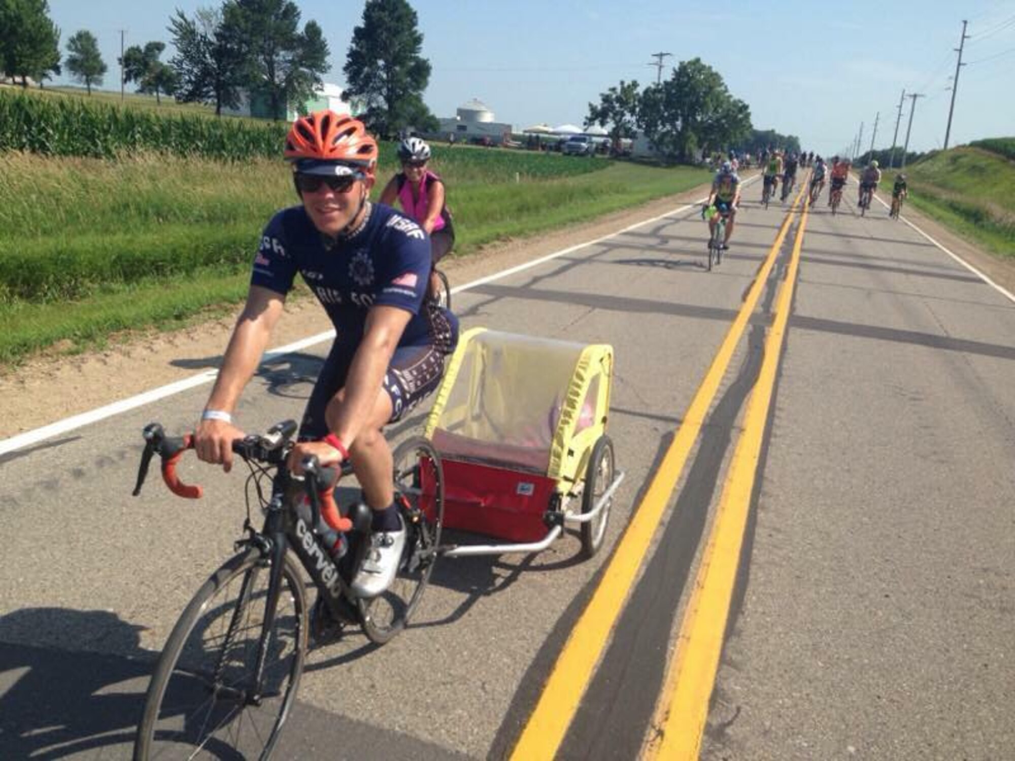 Senior Airman Jacob Pinkney, 860th Aircraft Maintenance Squadron C-17 Globemaster III crew chief and a member of the Air Force Cycling Team, pulls a toddler in a stroller carrier to give the child's mother a break during the Register's Annual Great Bike Ride Across Iowa July 26, 2017. During the RAGBRAI, AFCT members provided assistance to more than 5,000 cyclists. The team works to promote the Air Force by interacting with the American public at cycling events across the United States. (Courtesy Photo)