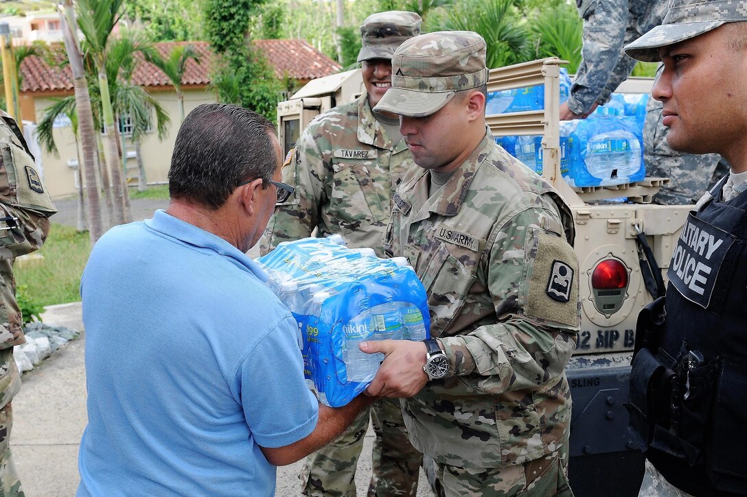 Soldiers pass a case of bottled water to a civilian.