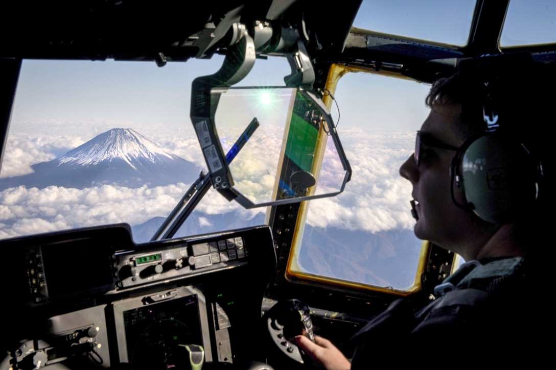 A pilot's cockpit window yields a view of Mount Fuji surrounded by clouds.
