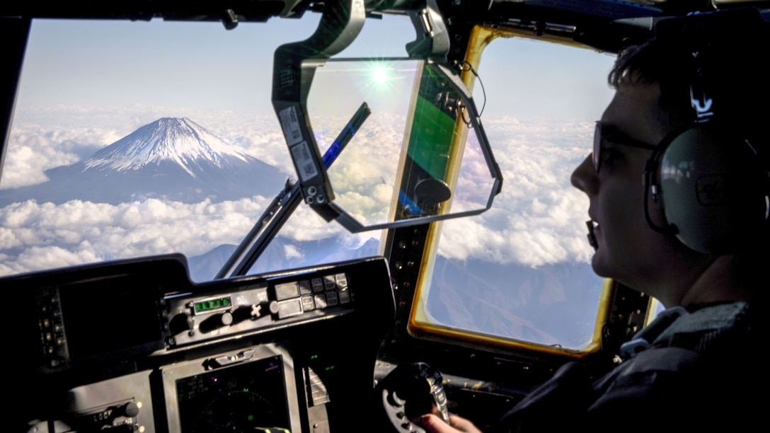 A pilot's cockpit window yields a view of Mount Fuji surrounded by clouds.