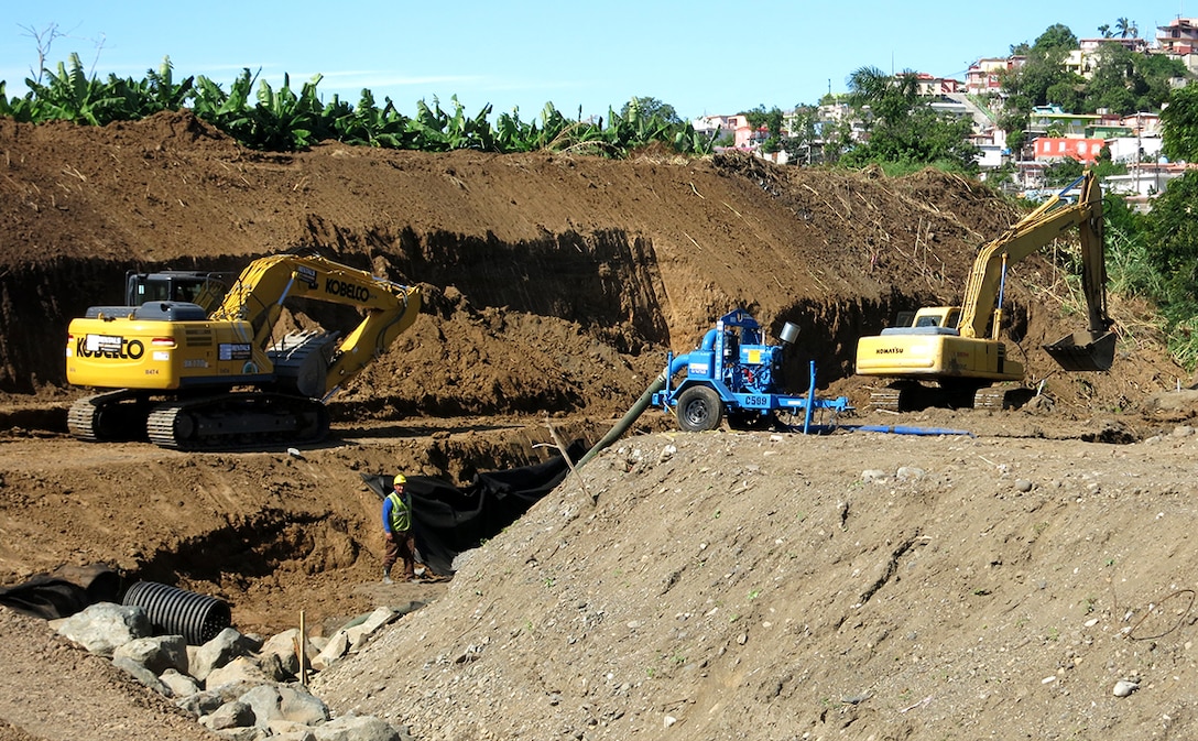A pump sitting on a temporary levee in Yauco, Puerto Rico, removes water as excavators place riprap in the early stages of construction of the new levee.