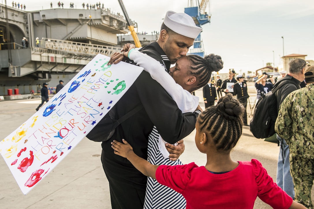 A sailor hugs his daughter while another runs toward him.