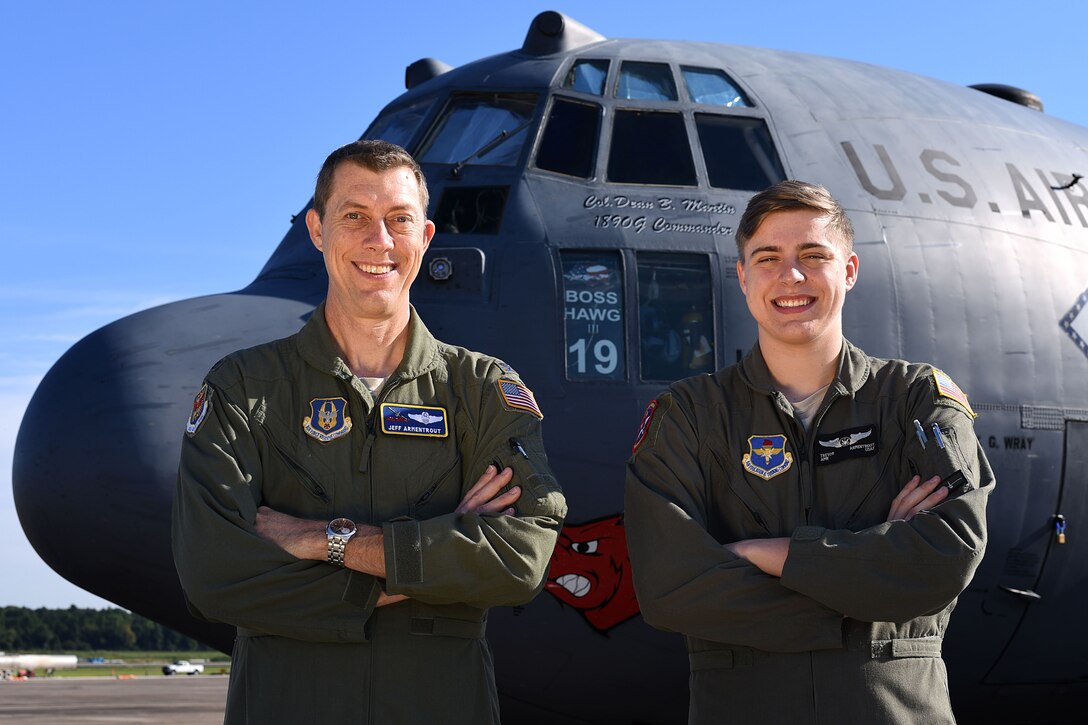 Airmen father and son stand next to each other in front of a c-130 military aircraft.