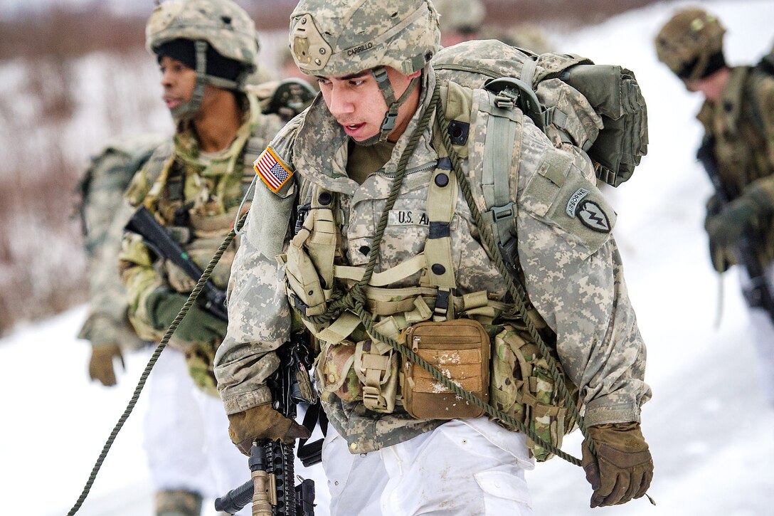 A soldier drags a stretcher with equipment on it while participating in parachute insertion and foot patrol training.