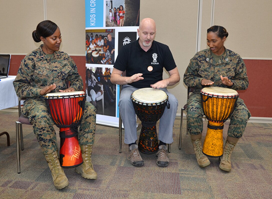 Two Marines play drums with a man.