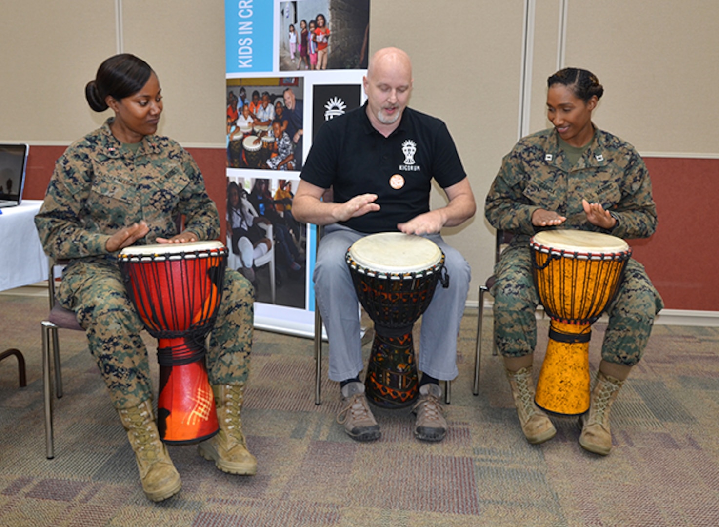 Two Marines play drums with a man.