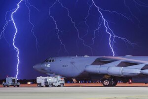 Lightning crosses the sky behind a military aircraft.