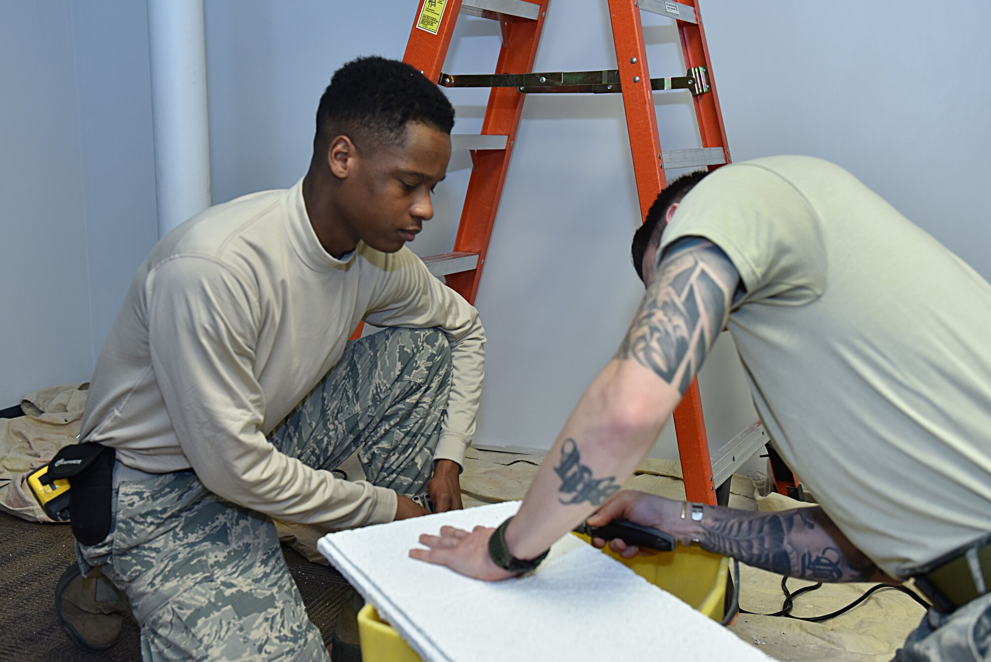 Senior Airman Terique Howard, left, structural engineering journeyman with the 911th Civil Engineering Squadron, observes a wingman as he cuts a piece of ceiling tile at the Pittsburgh International Airport Air Reserve Station, Dec. 3, 2017. The Airmen of the structures shop maintain the buildings across the base, enabling the mission by serving as the framework behind others. (U.S. Air Force photo by Staff Sgt. Marjorie A. Bowlden)