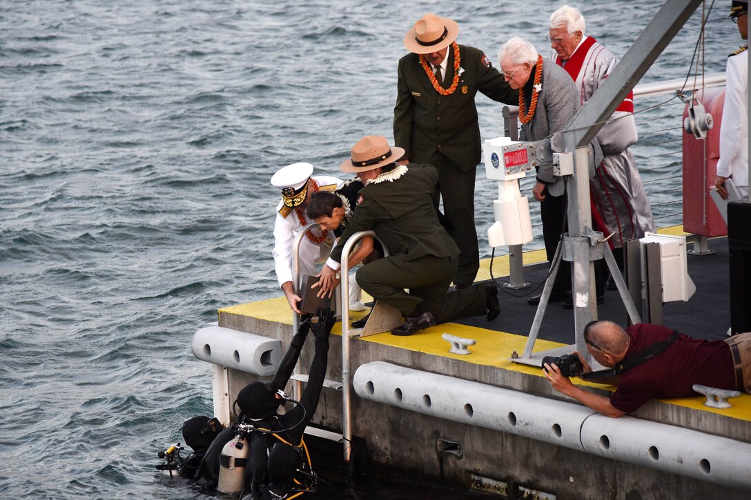 People kneeling on a pier deliver ashes to divers in water.