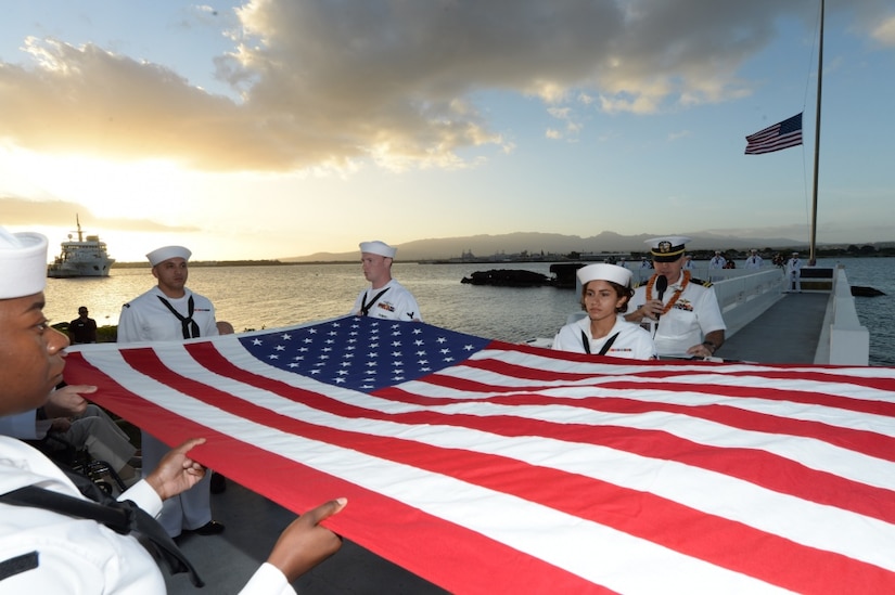 Sailors fold a large American flag during a commemoration ceremony.
