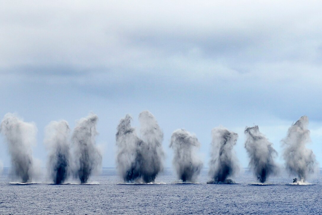Vertical splashes of water from ordinance dropped from aircraft create a "water wall" in the ocean.