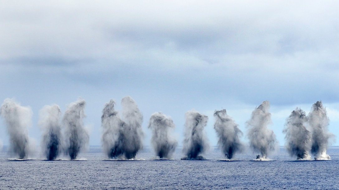 Vertical splashes of water from ordinance dropped from aircraft create a "water wall" in the ocean.