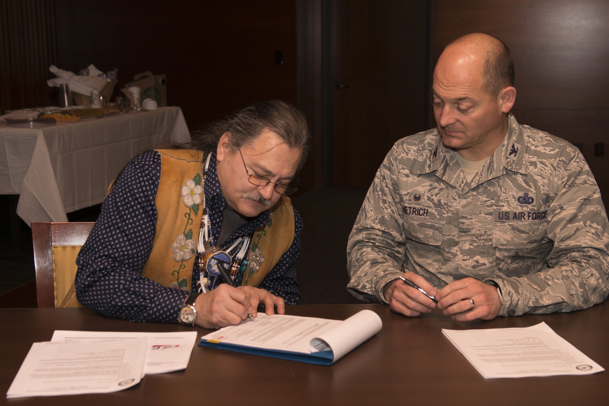 Gary Harrison, Chickaloon Native Village chief, and Air Force Col. George Dietrich, 673d Air Base Wing and Joint Base Elmendorf-Richardson commander, signs a memorandum of agreement at the Arctic Warrior Events Center at JBER, Alaska, Dec. 5, 2017. The MOA served to establish a relationship between JBER and the CNV to converse on mutual concerns, support and coordinate management of resources.