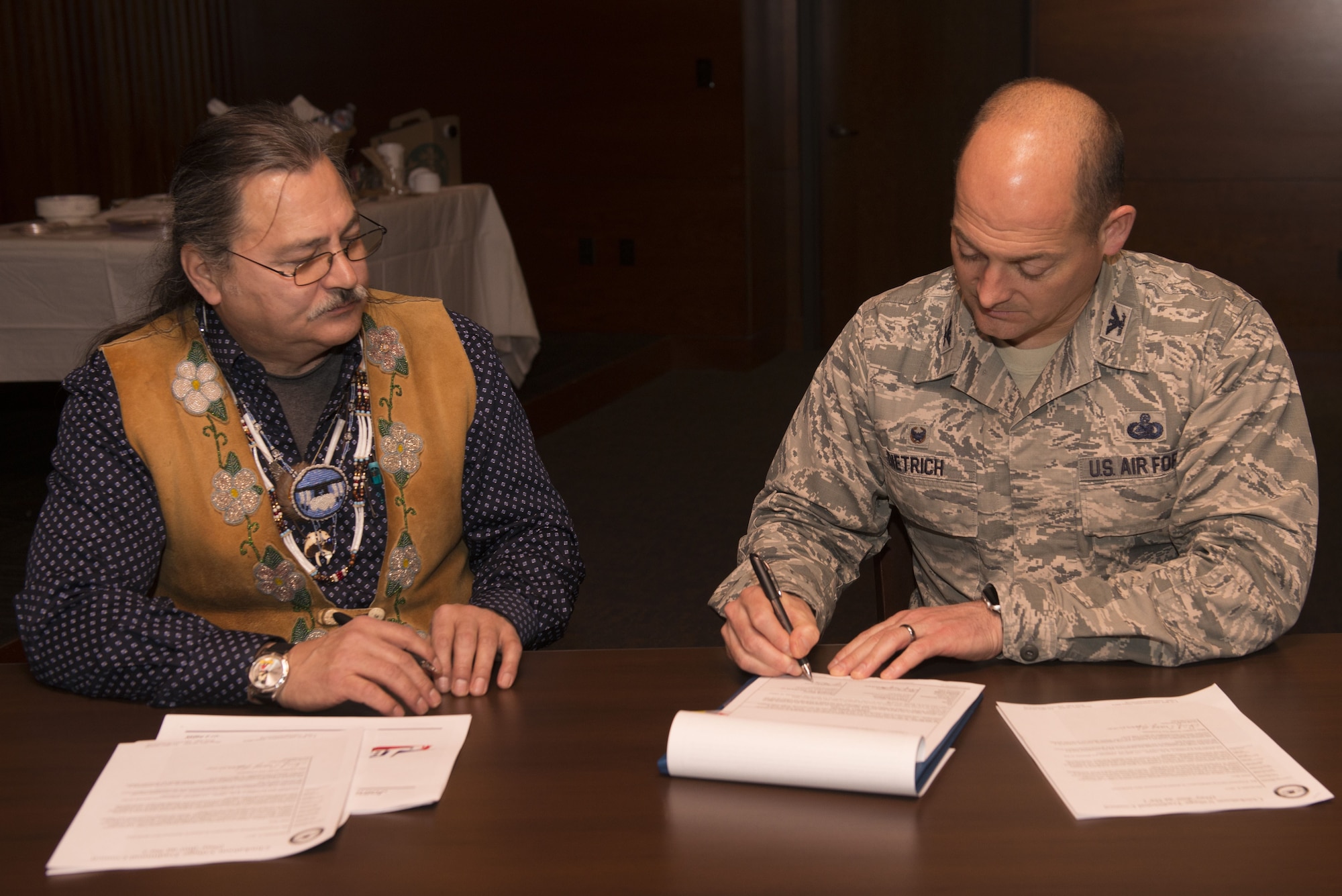 Air Force Col. George Dietrich, 673d Air Base Wing and Joint Base Elmendorf-Richardson commander, and Gary Harrison, Chickaloon Native Village chief, signs a memorandum of agreement at the Arctic Warrior Events Center at JBER, Alaska, Dec. 5, 2017. The MOA served to establish a relationship between JBER and the CNV to converse on mutual concerns, support and coordinate management of resources.